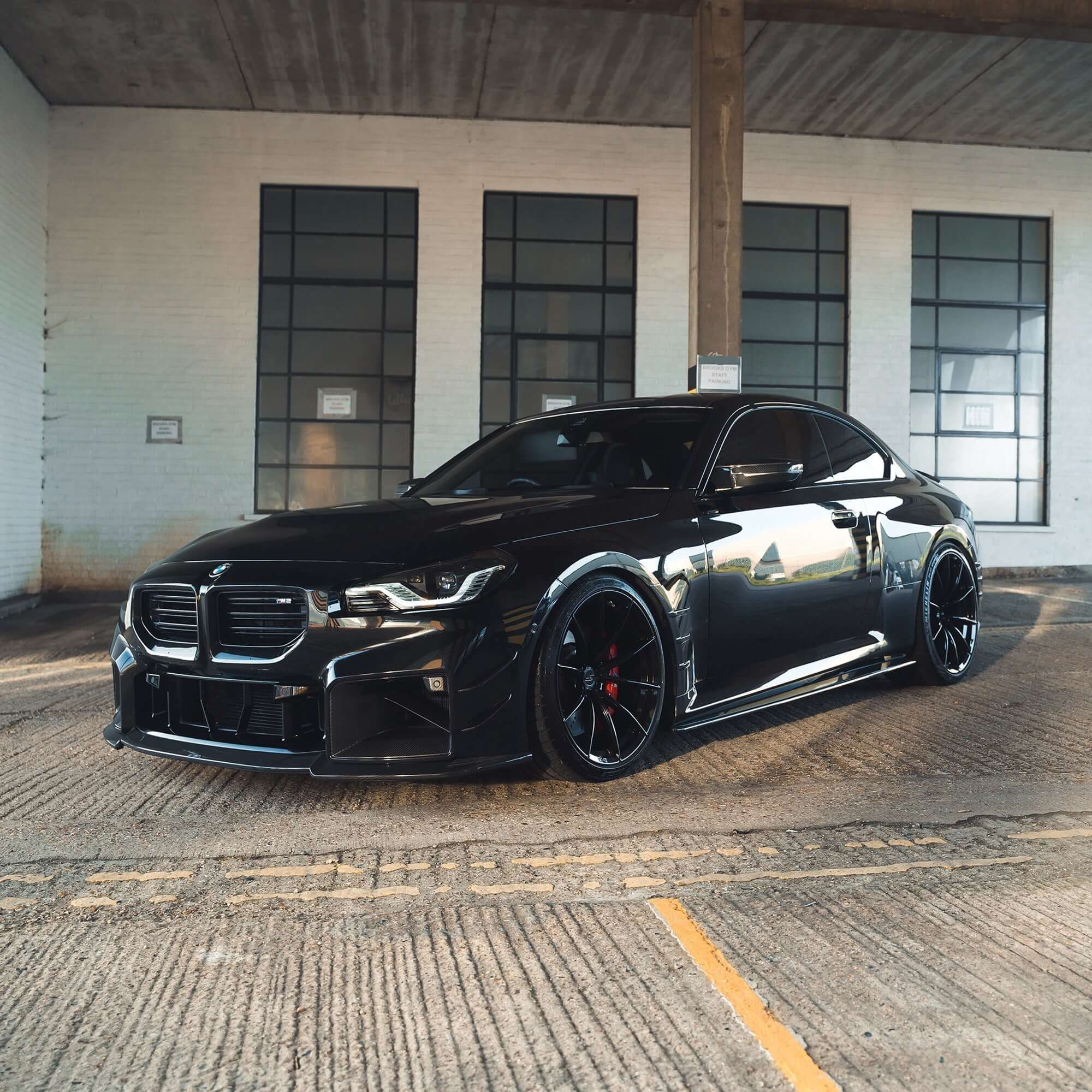 BMW G87 M2 Full Carbon Fibre Body Kit showcased on a sleek black BMW M2 in an industrial setting.