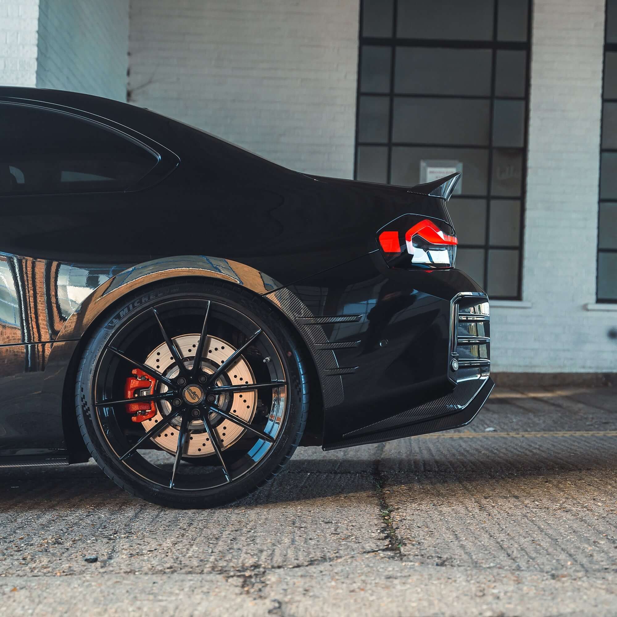 BMW G87 M2 Full Carbon Fibre Body Kit showcasing a sleek black car with stylish wheels and aggressive rear design.