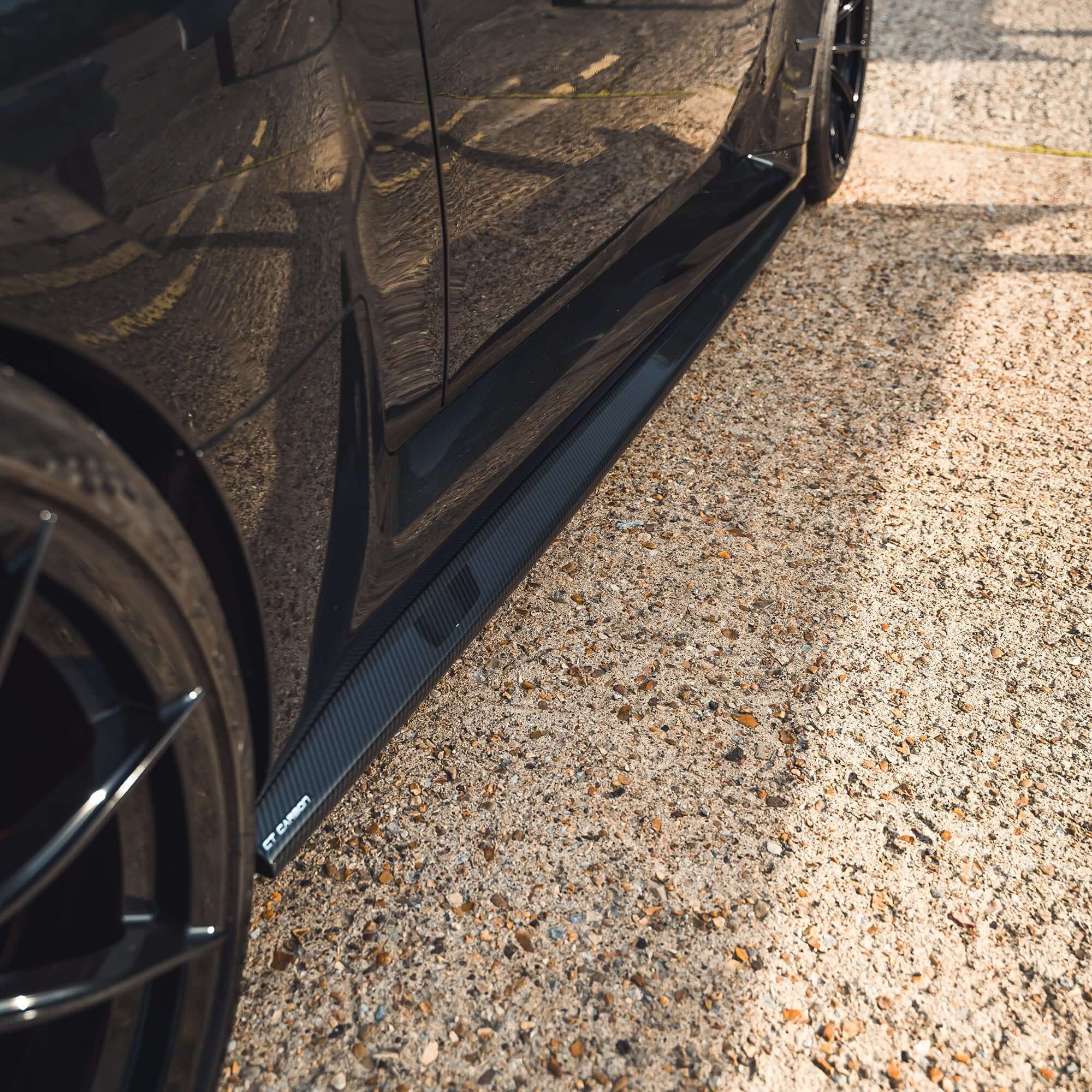 BMW G87 M2 Full Carbon Fibre Body Kit showcased on the side of a sleek black sports car.