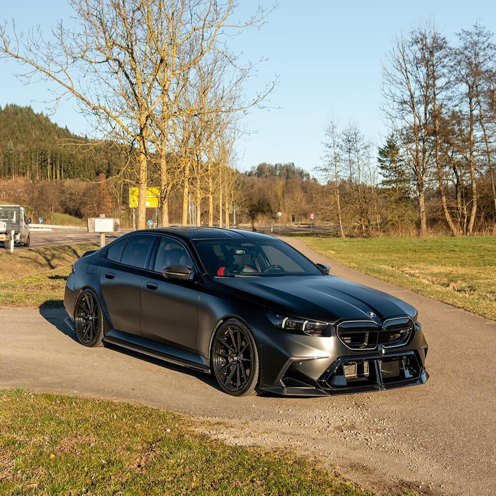 BMW G90 G99 M5 Carbon Fibre Front Splitter on a sleek black BMW M5 parked in a scenic outdoor setting.