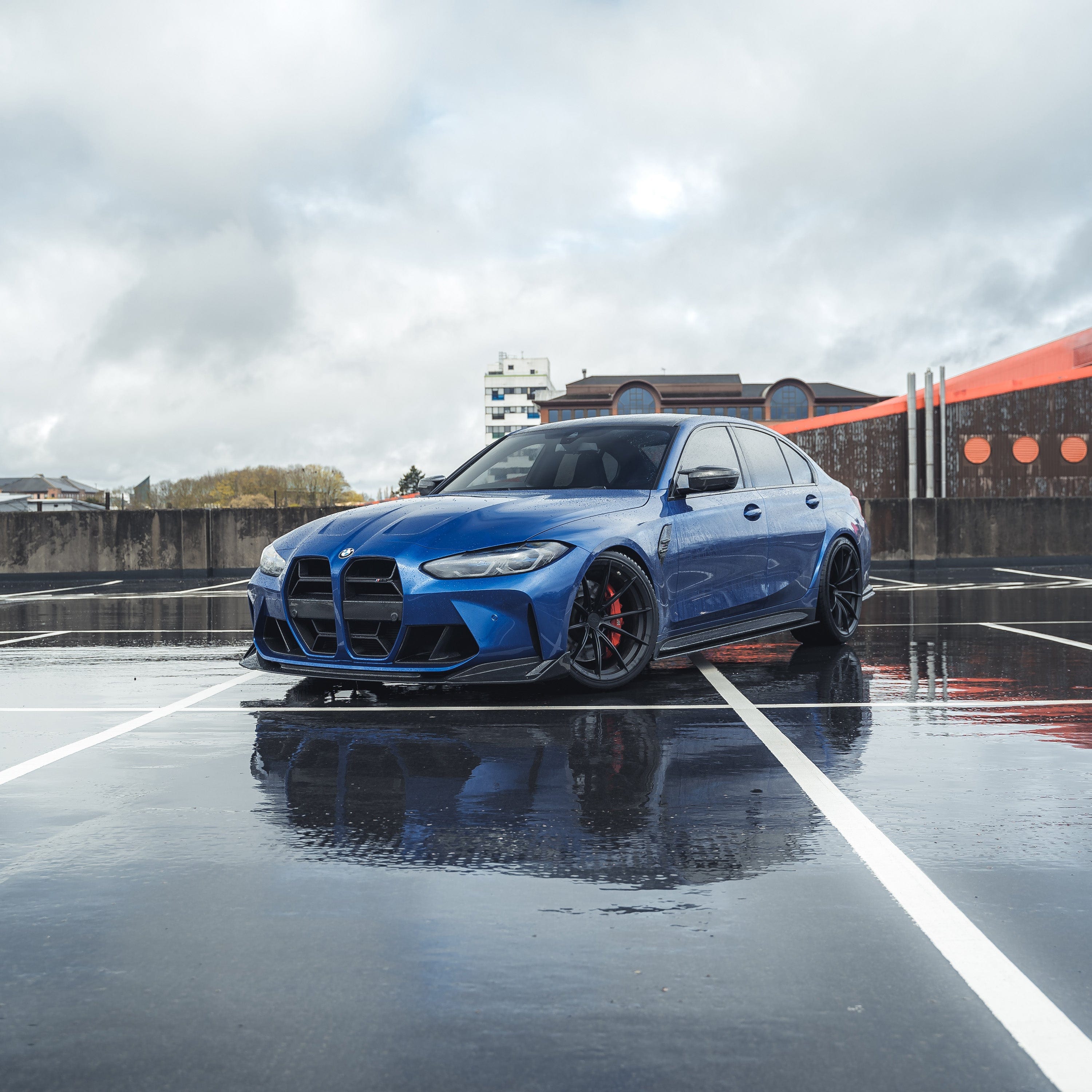 BMW M3 M4 carbon fibre splitter V2 on a blue BMW M3 parked in a wet parking lot.