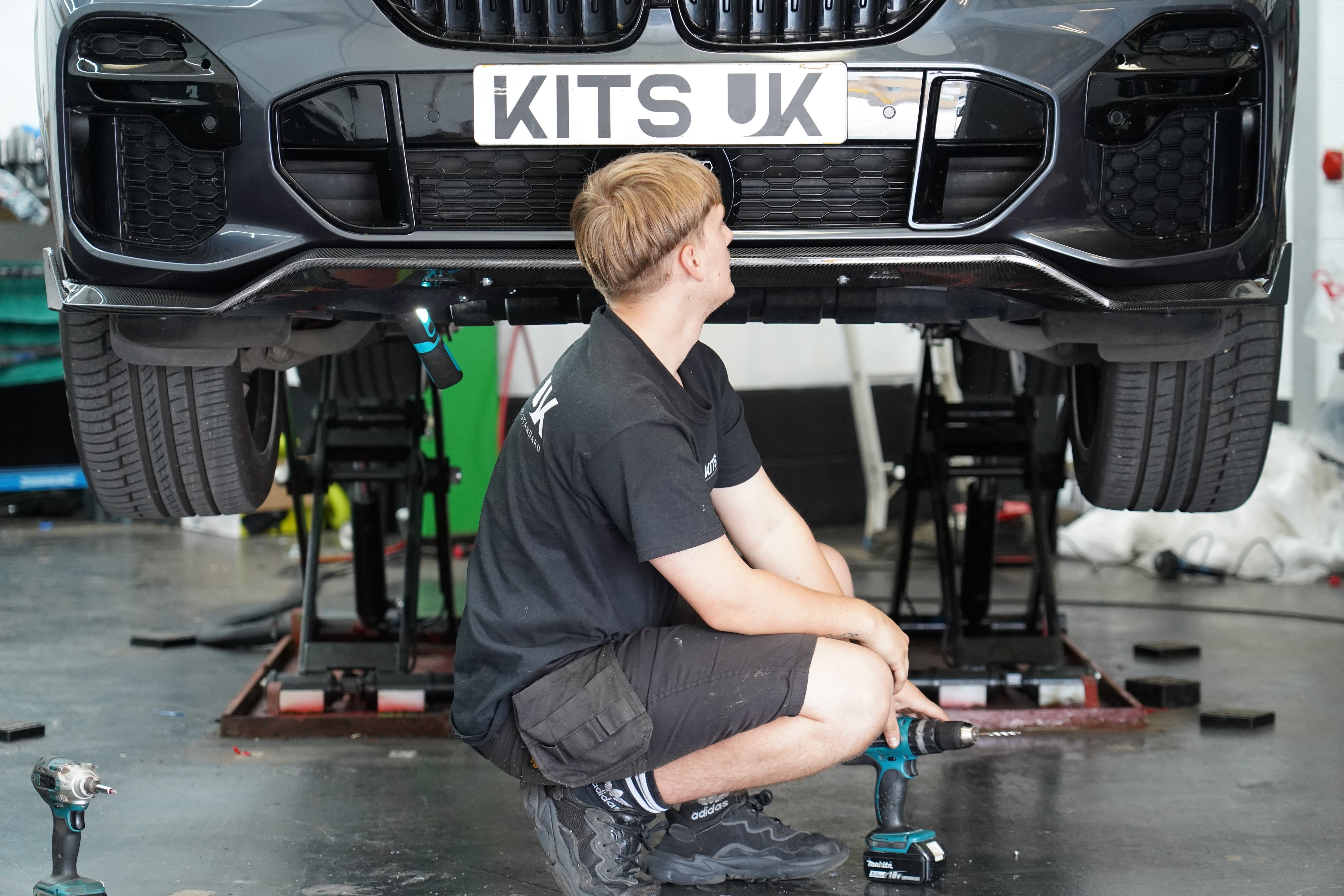 Mechanic working on a car with 'KITS UK' branding in a workshop.