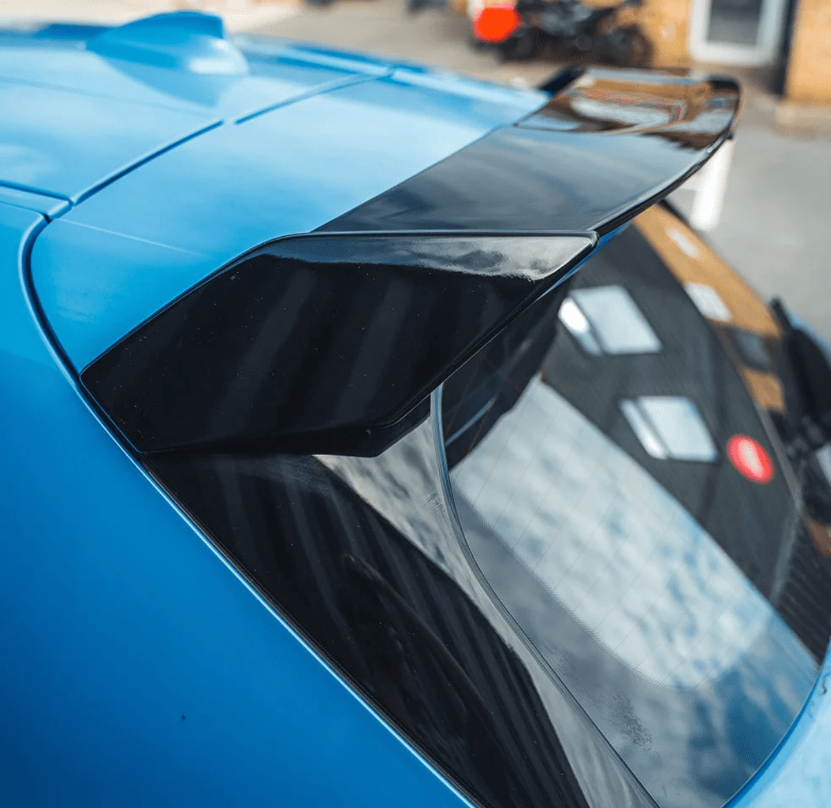 BMW F40 Roof Spoiler Gloss Black enhancing the rear profile of a blue car for improved aerodynamics.