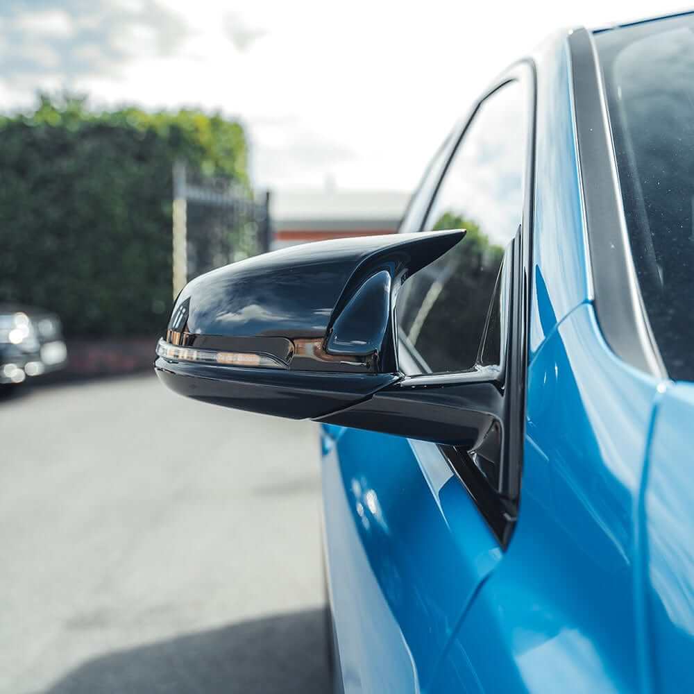 BMW F40 F44 gloss black mirror covers on a blue BMW vehicle side mirror viewed from the side.
