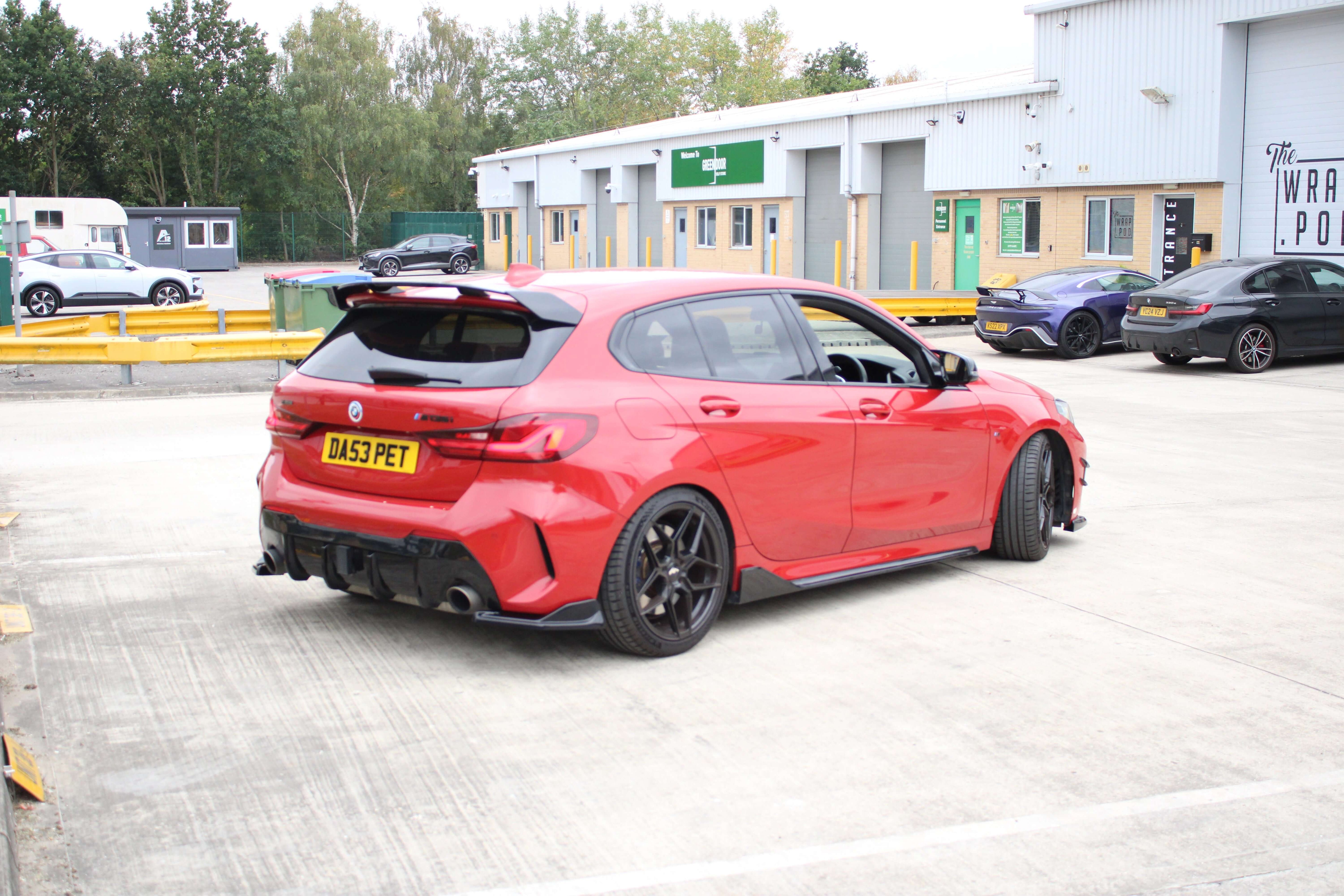 BMW F40 1 series - Gloss black side extentions on a red car parked in a commercial area.