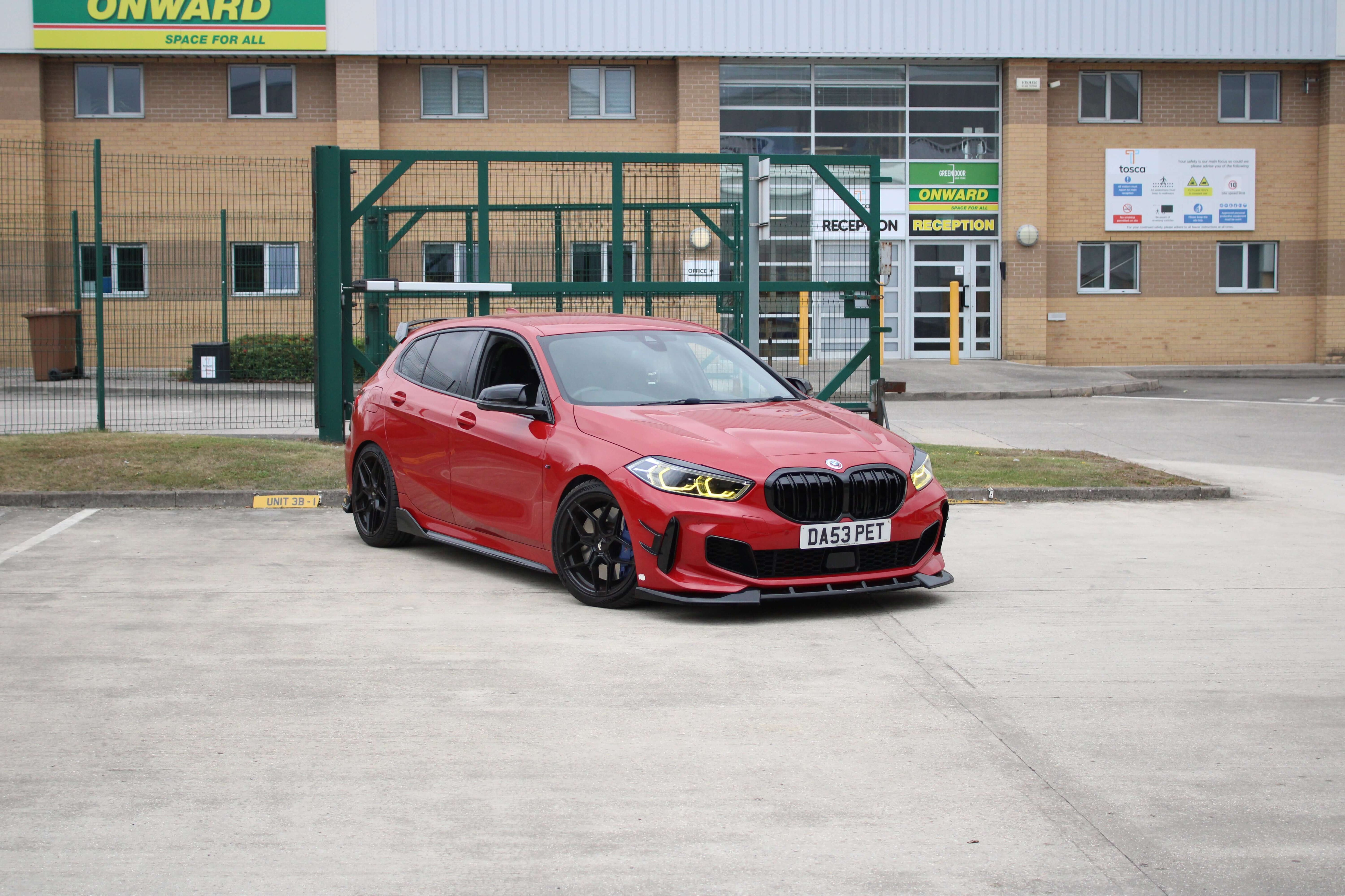 BMW Yellow DRL Modules on a red BMW hatchback parked outside a commercial building.