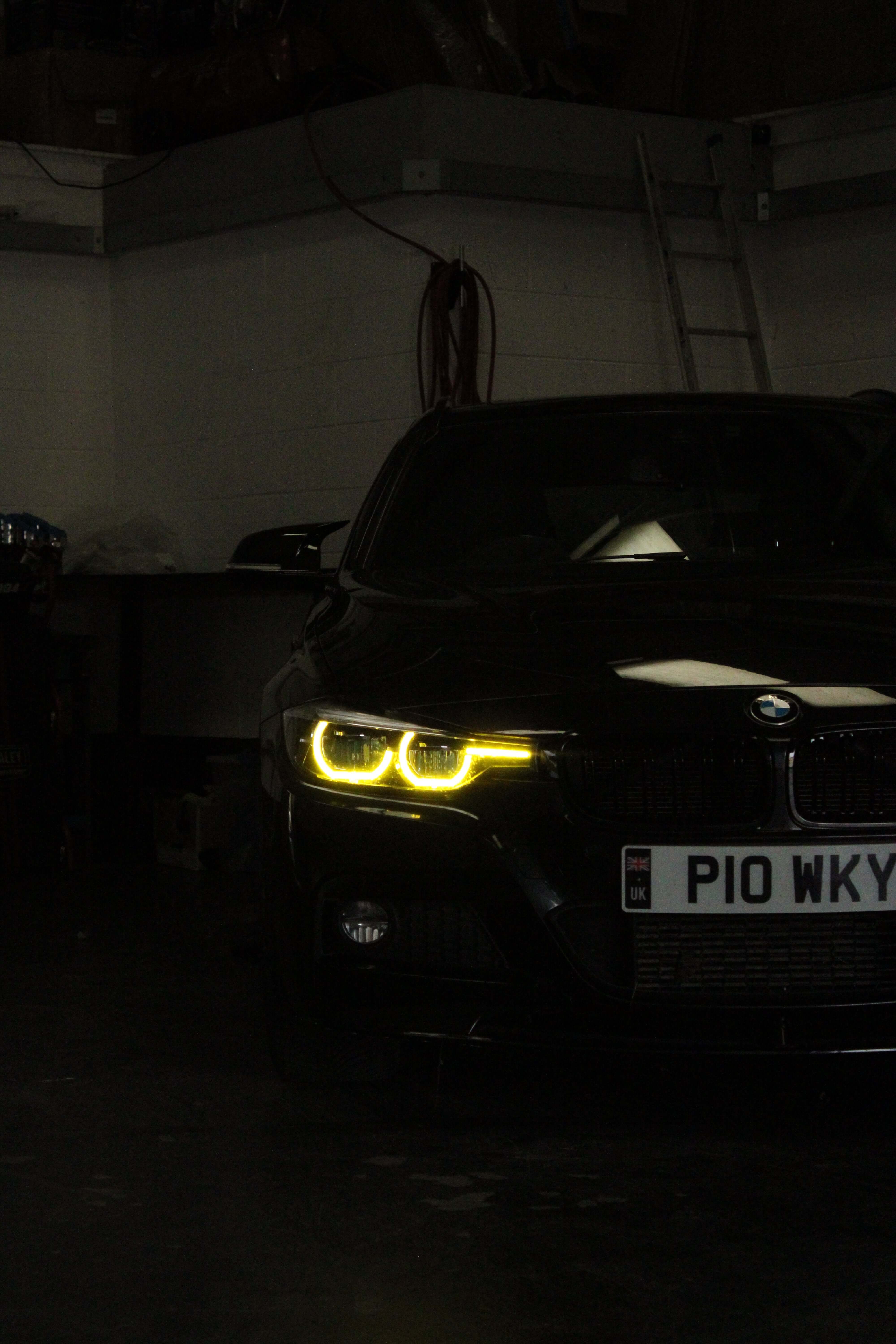 BMW Yellow DRL Modules illuminating on black BMW vehicle in a garage setting.