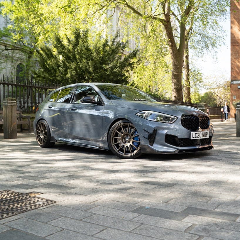 BMW F40 Carbon full body kit showcased on a grey BMW 1 Series parked in a scenic outdoor setting.