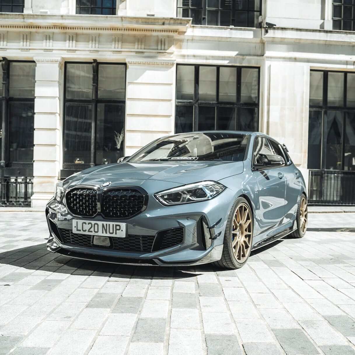 BMW F40 Carbon full body kit showcased on a sleek blue BMW 1 Series parked in an urban setting.