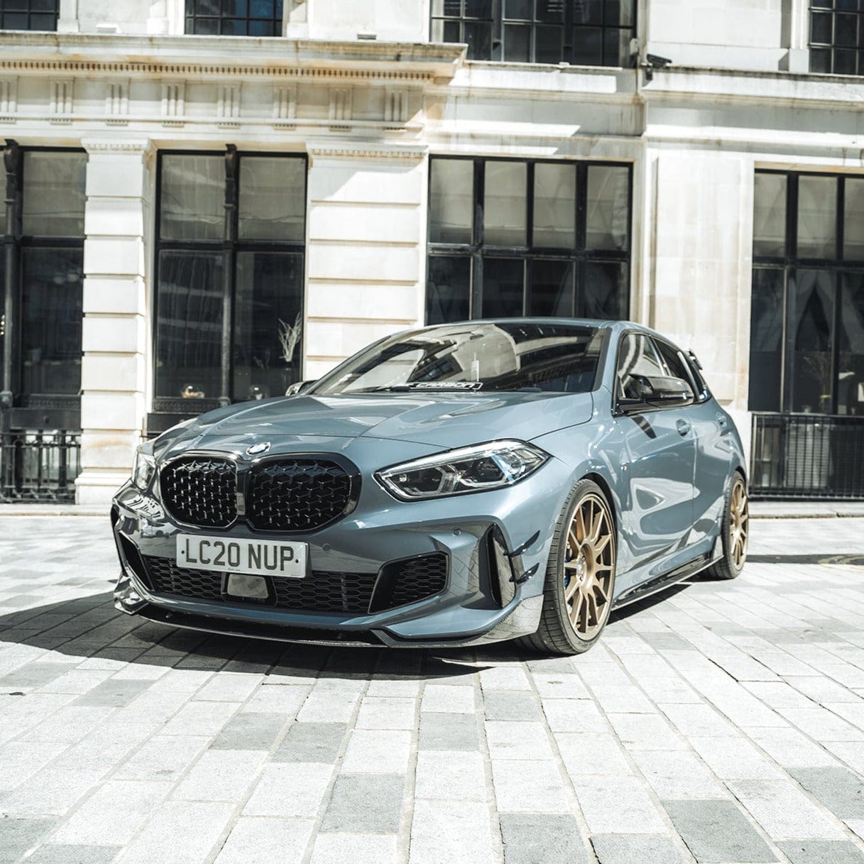 BMW F40 Carbon full body kit showcased on a sleek blue BMW 1 Series parked in an urban setting.