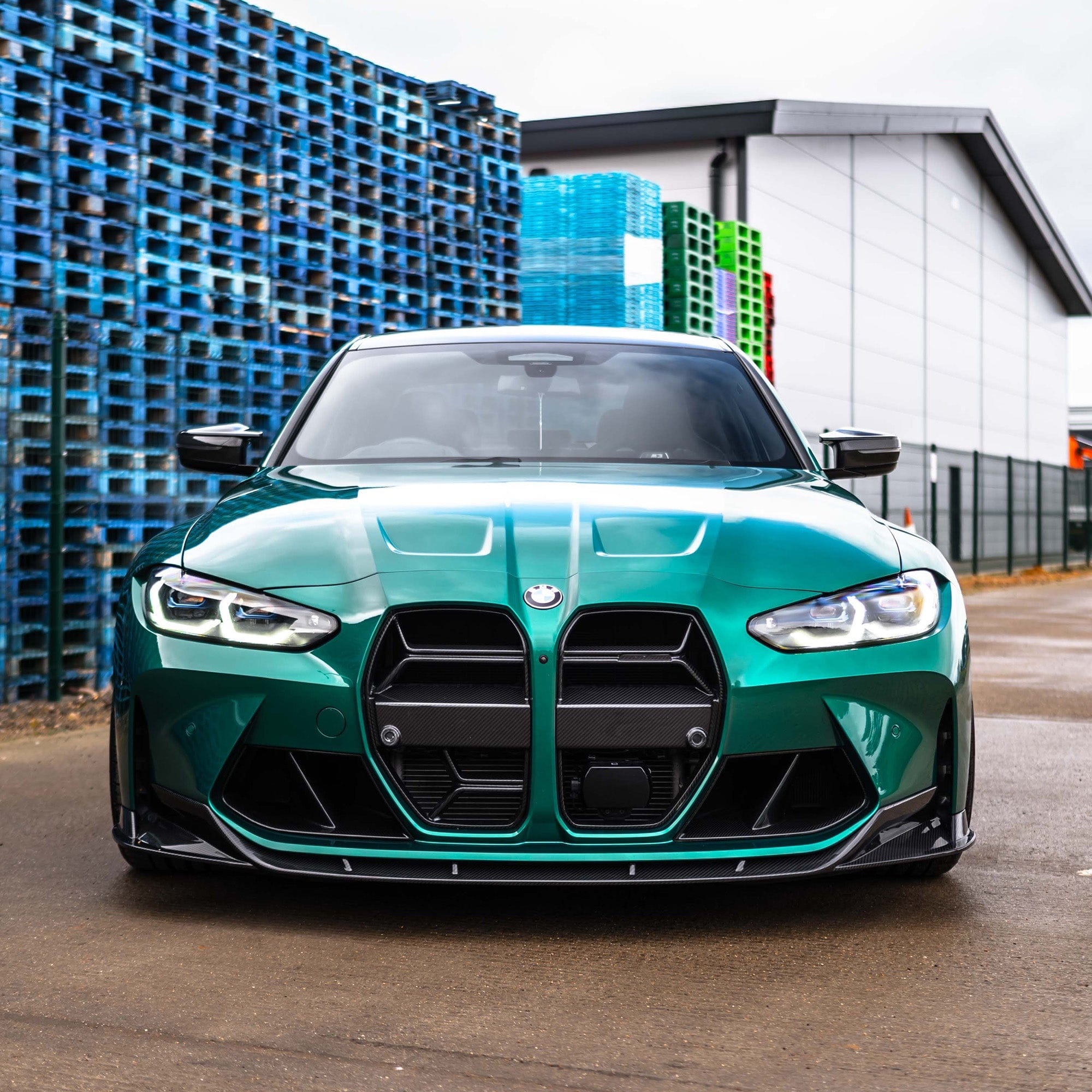 BMW G80 M3 carbon fibre splitter - V1 on a green car in an industrial setting.