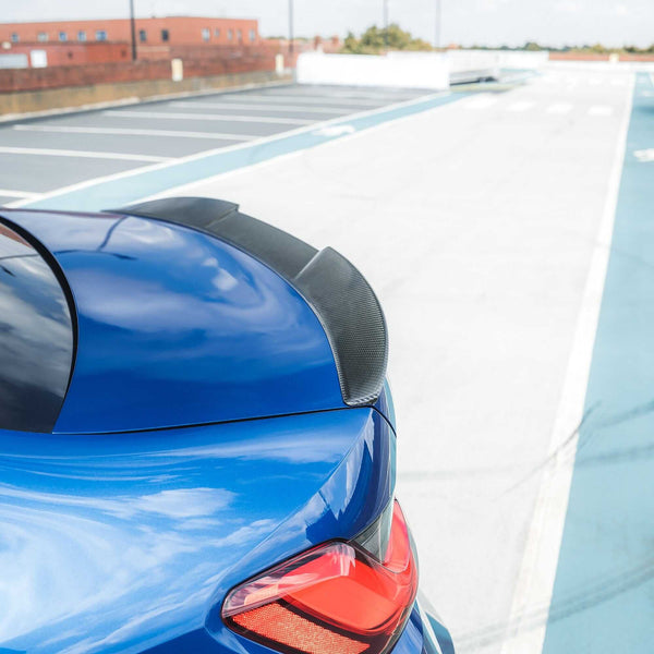 BMW G80 G20 carbon fiber spoiler enhancing rear profile of blue BMW vehicle in parking area.