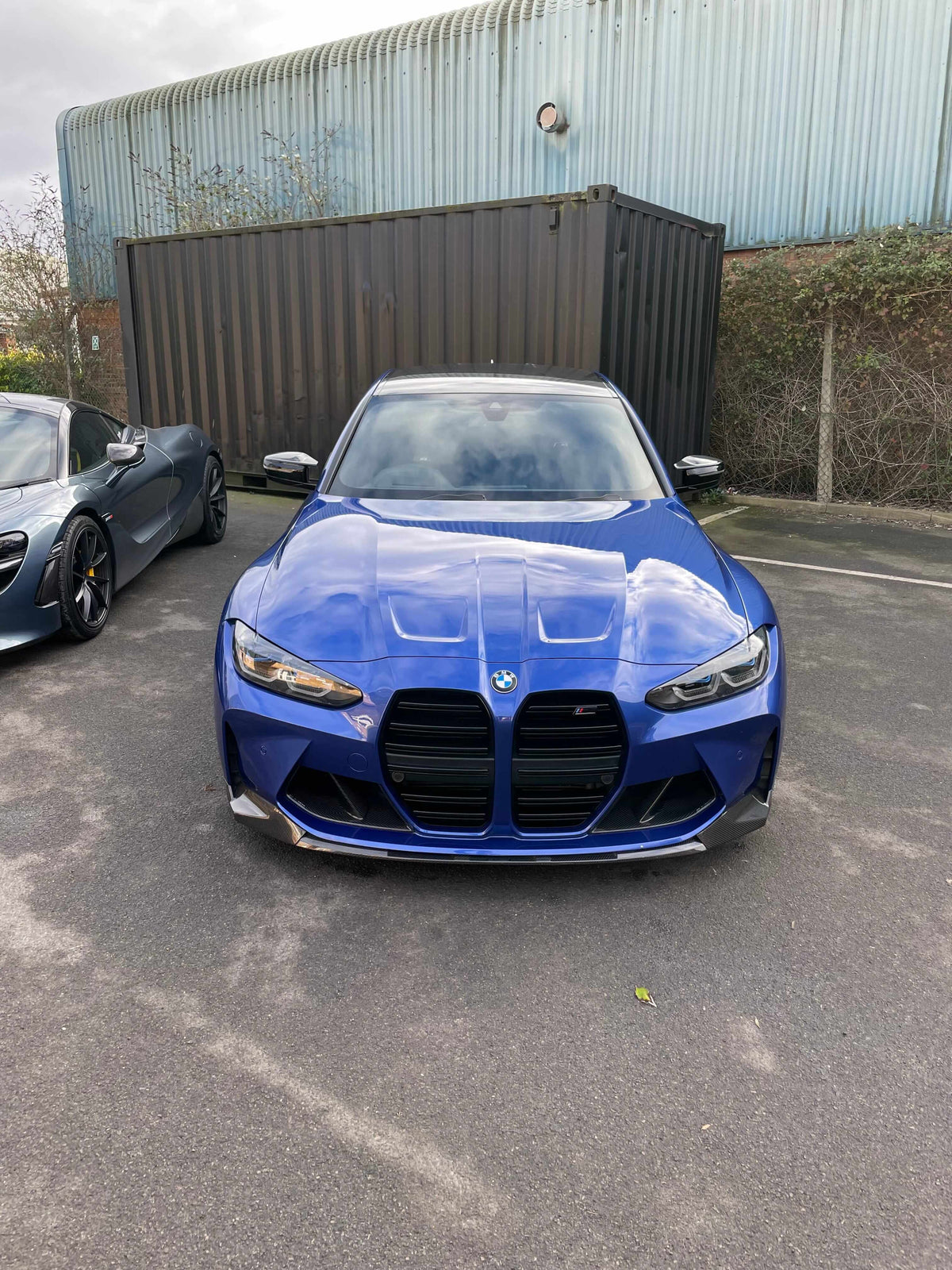 BMW G80 M3 FULL CARBON FIBRE KIT - MP STYLE displayed on a blue BMW M3 in front of a container.
